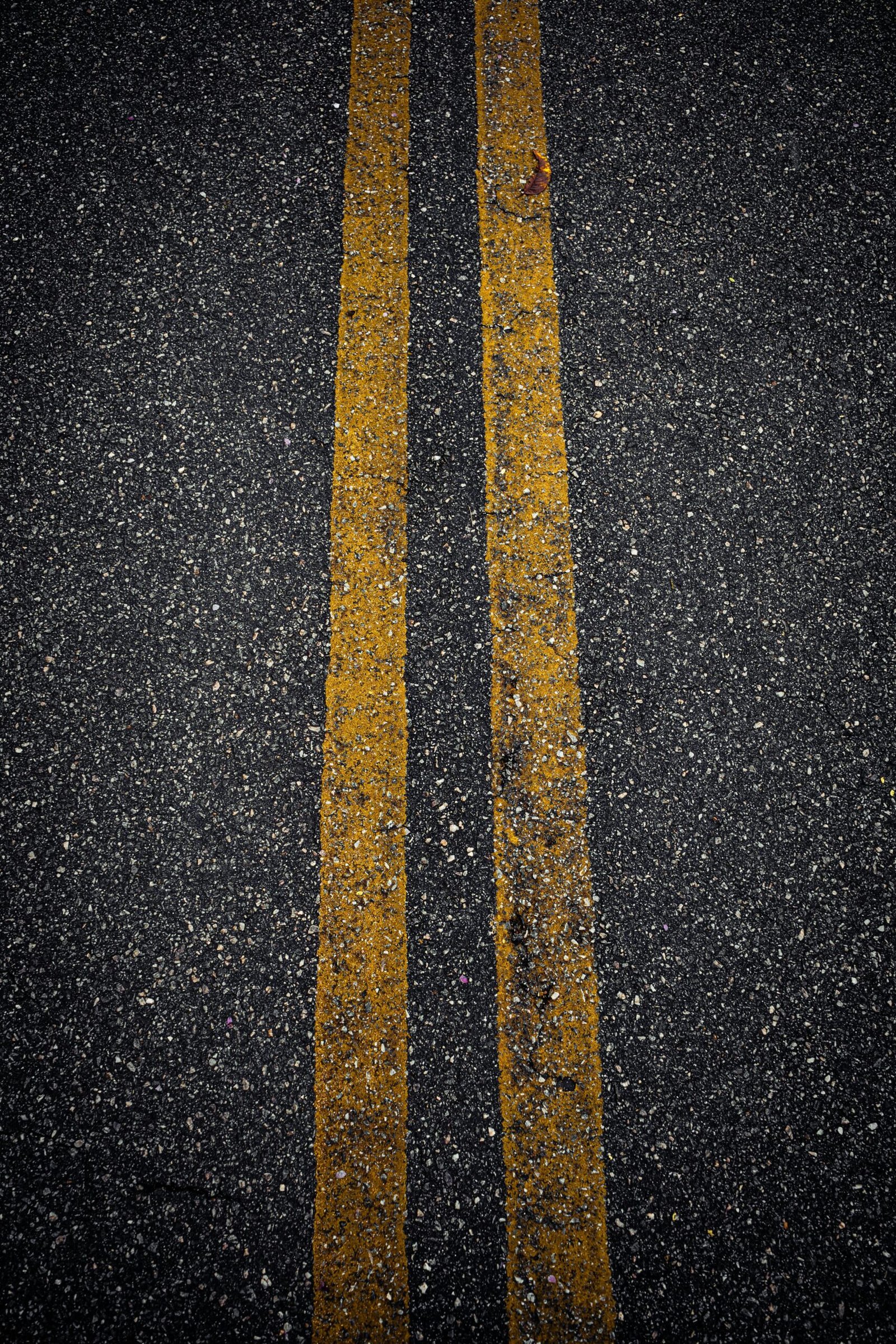 Detailed view of weathered double yellow lines on asphalt pavement, emphasizing urban texture.