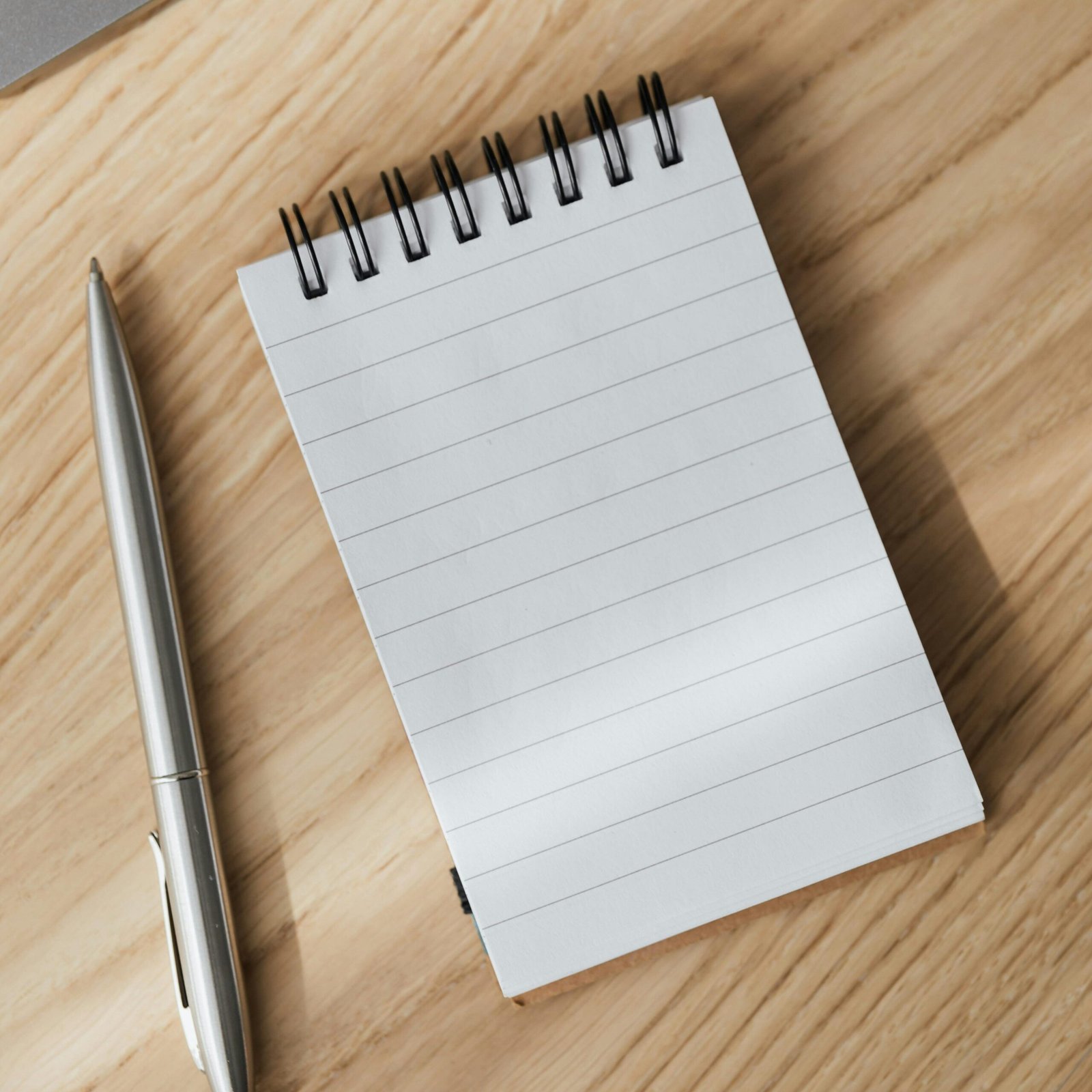 pexels-photo-4195410-4195410 From above of small opened notepad and stylish silver pen placed on wooden table near laptop